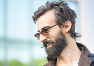 Portrait of hipster guy with confident face expression - Autumn fashion male model posing outdoors - Young man with beard and alternative mustache - Soft retro filter and shallow depth of field